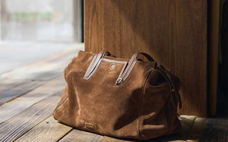 Brown suede tote bag on a wooden floor near a window