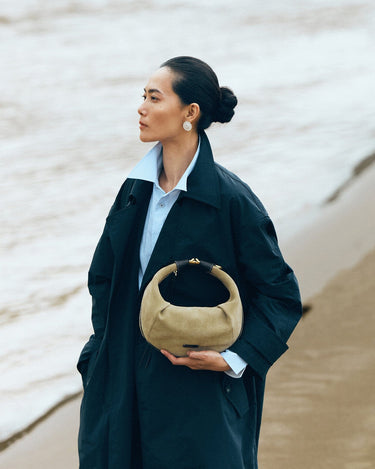 Medium Luna Hobo Bag in Dune Suede held by a woman on a beach