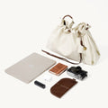 Light ivory medium gather bag with laptop, camera, earbuds, notebook, and leather case.