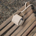 Songmont full-grain leather AirPods case in beige with magnetic closure and embossed logo.