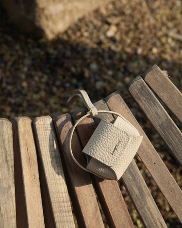 Beige textured full-grain leather Songmont AirPods case with magnetic closure on a wooden bench.