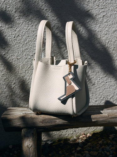Cream pebble-grain leather handbag with a playful dog-shaped charm dangling from the handle.