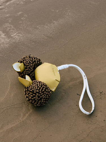 Yellow leather crab charm with textured brown body and white strap on sand