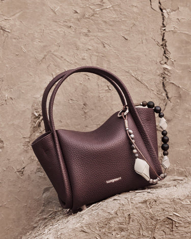 Small Carefree Thread Charm bag in plum, featuring pebbled leather, 'Songmont' logo, and beaded charm.