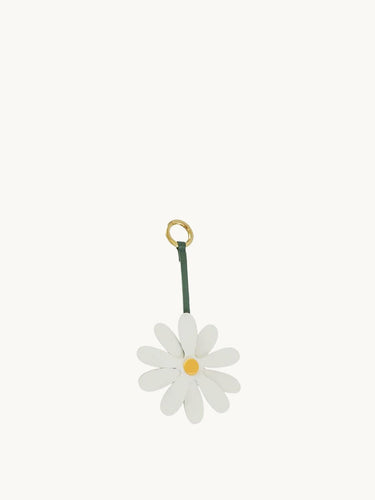 White leather daisy charm with yellow center on a green strap and gold ring.