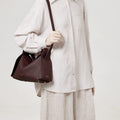 Burgundy leather Drippy Roof Bag with gold hardware, worn by a model in a light-colored linen outfit.
