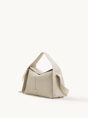 Light beige full-grain leather Drippy Roof Bag with textured finish, flap closure, and adjustable strap.