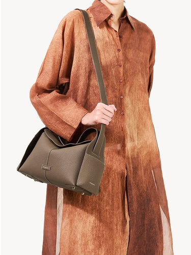 Taupe textured leather Drippy Roof Bag with adjustable strap, held by a person in a brown garment.