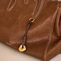 Faith Stone Charm bag in Sandal color, vegetable-tanned leather with white stitching and gold hardware.