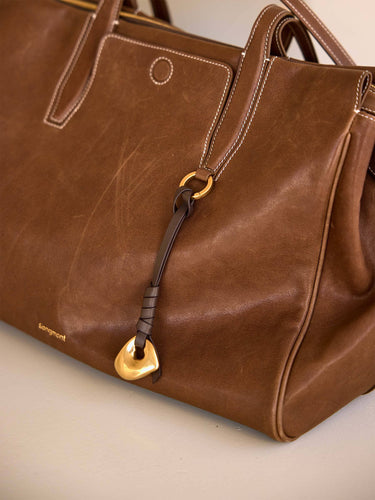 Faith Stone Charm bag in Sandal color, vegetable-tanned leather with white stitching and gold hardware.