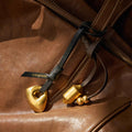 Faith Stone Charm accessory for a brown leather bag, featuring golden stone-like and cylindrical charms with beaded accents.