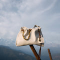 Songmont Gather Clutch Set in Cloud color. Soft leather clutch with beaded strap, displayed outdoors with mountain scenery.