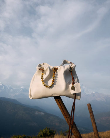 Songmont Gather Clutch Set in Cloud color. Soft leather clutch with beaded strap, displayed outdoors with mountain scenery.