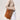 Large caramel suede Drippy tote bag with leather logo tag, worn on shoulder by a woman in beige top and light jeans.