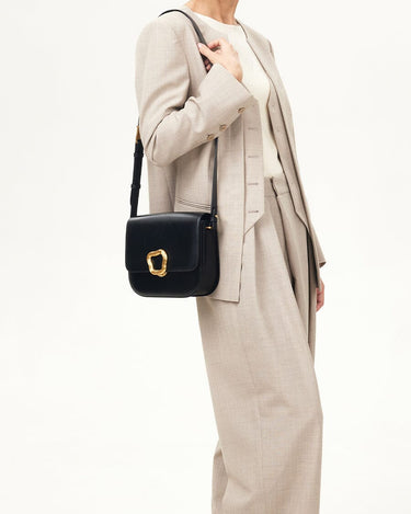 Onyx black calf leather crossbody bag with gold Wonton ring closure worn by a woman in a light beige suit.