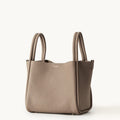 Songmont large leather bucket bag in taupe with double top handles and a minimalist design.