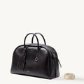 Dark brown Yore bowling bag in full-grain Nappa leather with white stitching and top handles. Includes a detachable patterned strap.