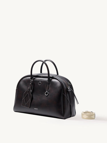 Dark brown Yore bowling bag in full-grain Nappa leather with white stitching and top handles. Includes a detachable patterned strap.