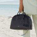 Large navy full-grain leather Yore bowling bag with white stitching, held on a beach.