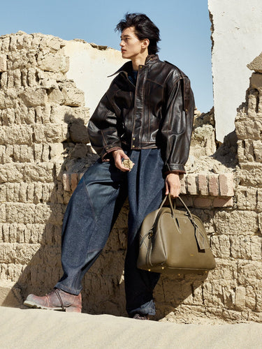 Large Yore Bowling Bag in Moss with white contrast stitching, held by a man in a leather jacket and wide-leg jeans.