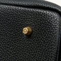 Close-up of a black full-grain leather tote bag showing its pebbled texture and a brass snap with 'Songmont' embossed.