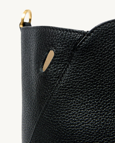 Close-up of the textured black leather of the Large Yore Tote Bag, showing a golden ring detail and a subtle cutout.