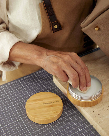 Person applying Leather Care Balm with a cloth from a bamboo container. Includes "songmont" logo.