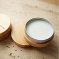Leather care balm in a tin with a bamboo lid and base, on a textured stone surface.