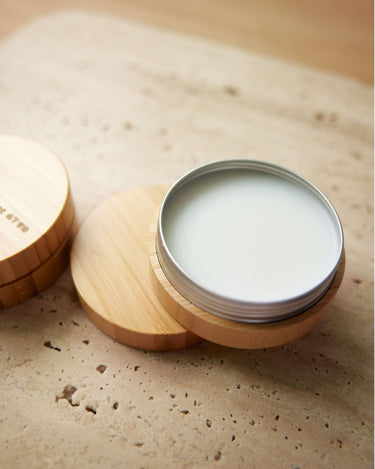 Leather care balm in a tin with a bamboo lid and base, on a textured stone surface.
