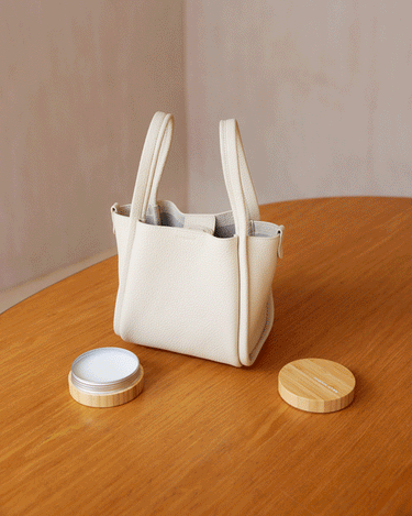 Cream leather handbag with beeswax care balm on a wooden table, perfect for leather care.