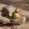 Cypress Lucky Gourd Charm with braided cords and gold accents on a stone.