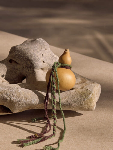 Cypress Lucky Gourd Charm with braided cords and gold accents on a stone.