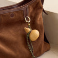 Brown suede Songmont bag with lucky gourd charm and braided cords.