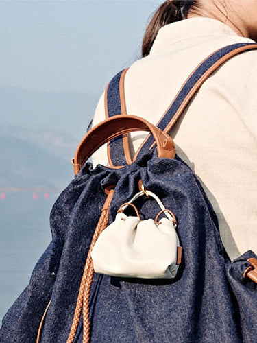 White leather Lucky Pouch Charm with adjustable strap, attached to a denim backpack.