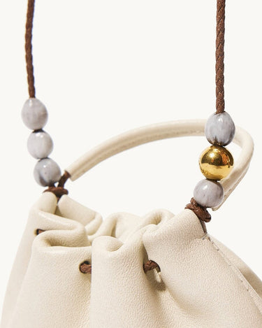 Cream full-grain nappa leather pouch charm with adjustable strap, featuring grey and gold bead accents.
