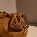 Brown suede leather pouch charm attached to a larger suede bucket bag