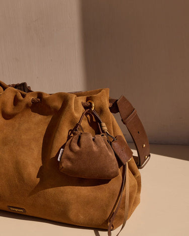 Brown suede leather pouch charm attached to a larger suede bucket bag