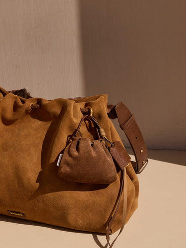 Brown suede leather pouch charm attached to a larger suede bucket bag