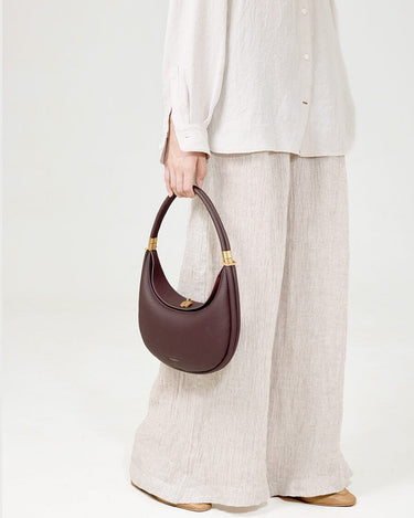 Burgundy Luna Bag with gold hardware, made of textured leather, and an adjustable strap.