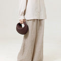 Burgundy Luna Bag made of full-grain leather, held by a person wearing a linen shirt and wide-leg pants.