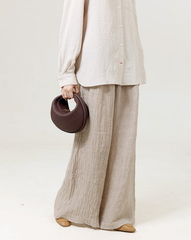 Burgundy Luna Bag made of full-grain leather, held by a person wearing a linen shirt and wide-leg pants.