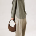 Chocolate pebbled leather Luna Bag with gold hardware, worn with a green shirt and tan pants.