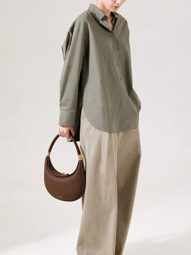 Chocolate pebbled leather Luna Bag with gold hardware, worn with a green shirt and tan pants.
