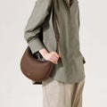 Chocolate Luna Bag crafted from pebbled leather with gold hardware, worn crossbody by a model.