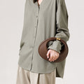 Brown pebbled leather Luna Bag with gold clasp, held by a person in an olive shirt and beige pants.