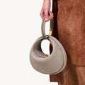 Luna Bag in Cobble: Textured pebble-grain leather handbag with gold hardware, held by a person wearing brown.