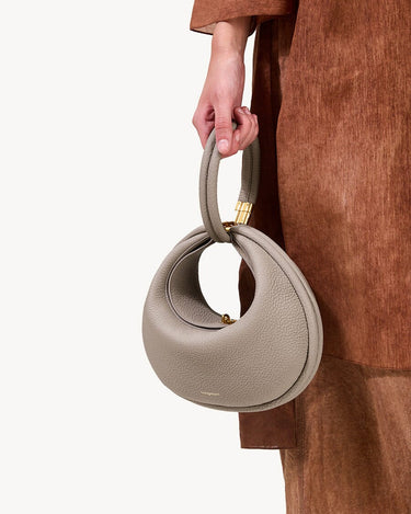 Luna Bag in Cobble: Textured pebble-grain leather handbag with gold hardware, held by a person wearing brown.
