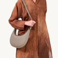 Luna Bag in Cobble textured leather with adjustable strap, worn by a model in a flowing brown dress.