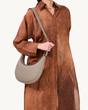 Luna Bag in Cobble textured leather with adjustable strap, worn by a model in a flowing brown dress.