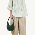 Emerald green pebbled leather Luna Bag with gold hardware, worn with light green blouse and beige pants.